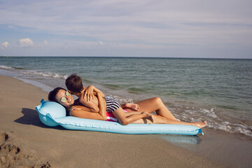 mom and son are lying on the beach on inflatable blue mattress during the summer vacation