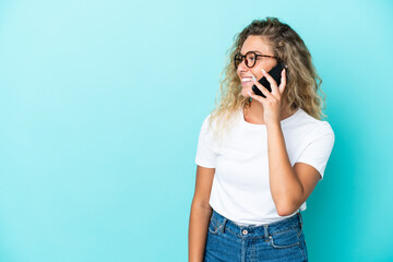 Girl with curly hair isolated on blue background keeping a conversation with the mobile phone with someone