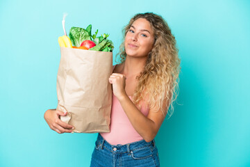 Girl with curly hair holding a grocery shopping bag isolated on green background proud and self-satisfied