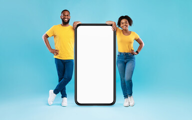 African American couple leaning on giant smartphone with mockup, promoting app or website, advertising your service