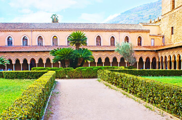 The trimmed bushes and lush palms in garden of Monreale Cloister, Sicily, Italy