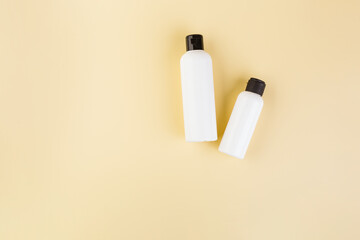 Two plastic bottles of different size on light yellow. No label. Close up, top view, copy space for text or logo.