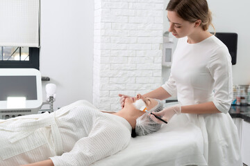 Mature woman receiving wwhte facial mask in spa beauty salon. Concept of skin care for older people