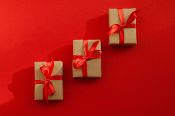 gifts in craft packaging with red ribbons on a red background with a shadow