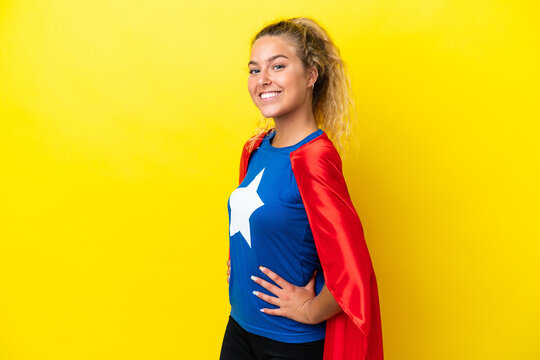 Girl with curly hair isolated on yellow background in superhero costume and doingposing with arms at hip and smiling