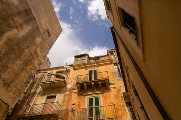 Fototapeta na wymiar City landscape of Sicilian Ragusa Ibla old town. Sandstone houses, balconies, nobody on the street. Bright sunny view from below photo good for touristic booklets, travel company website, posters etc