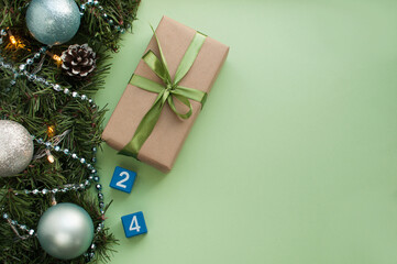 a gift with a green ribbon and the numbers 2 and 4 on blue cubes on a green background with a Christmas edge