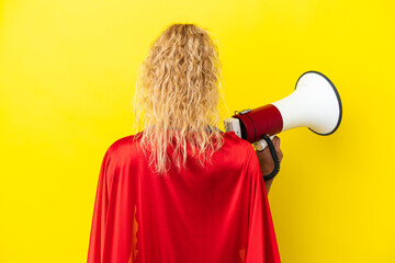 Super Hero woman isolated on yellow background holding a megaphone and in back position