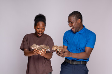 young african man and woman looking surprised and excited holding a lot of money