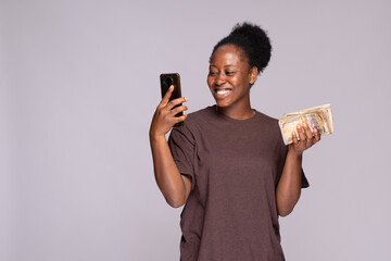 happy young african woman holding a lot of money and using her phone