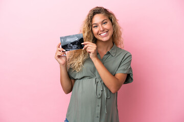 Girl with curly hair isolated on pink background pregnant and holding an ultrasound