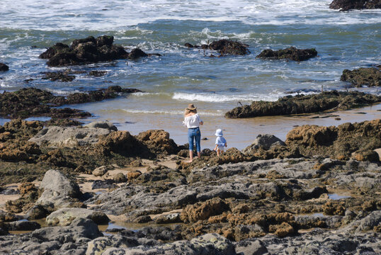 M&atilde;e e filha beb&eacute; juntas na praia perto da &aacute;gua do mar, paradas a observar a &aacute;gua, fam&iacute;lia, proteger, protec&ccedil;&atilde;o