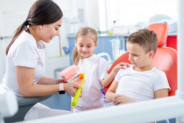 Obraz na płótnie Canvas pediatric dentist shows young children how to brush their teeth properly. Children - a boy and a girl in doctor's office. concept is health of children's teeth.