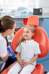 pediatric dentist talks to a little girl and tells her how to take care of her teeth. beautiful girl is smiling in dentist's office. concept is a children's medical examination.