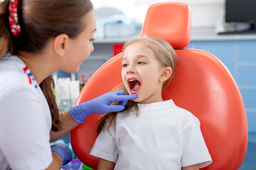 pediatric dentist talks to a little girl and tells her how to take care of her teeth. beautiful girl is smiling in dentist's office. concept is a children's medical examination.