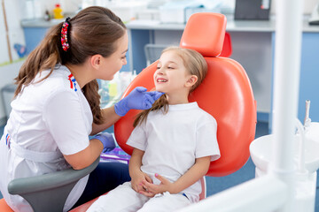 pediatric dentist talks to a little girl and tells her how to take care of her teeth. beautiful girl is smiling in dentist's office. concept is a children's medical examination.
