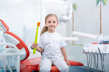 child girl in white clothes at reception at a pediatric dentist smiles and laughs. little girl...