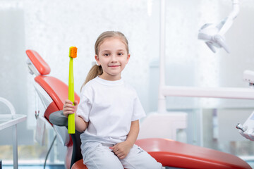 child girl in white clothes at reception at a pediatric dentist smiles and laughs. little girl...