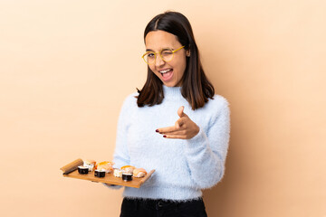 Young brunette mixed race woman holding sushi over isolated background pointing to the front and smiling