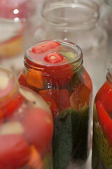 red tomatoes and cucumbers in a glass jar with pickle for canning against the background of empty glass jars in a vertical format