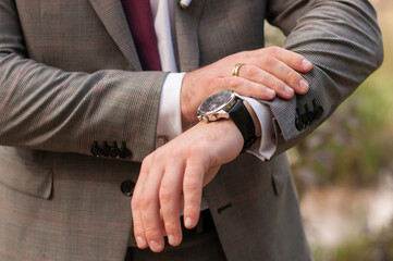 a man in a classic gray suit and a white shirt and tie looks at his wristwatch