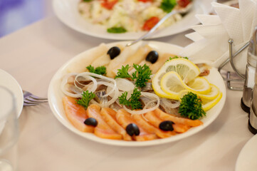 a dish of several types of salted fish with onion rings on top in a white plate on a set table