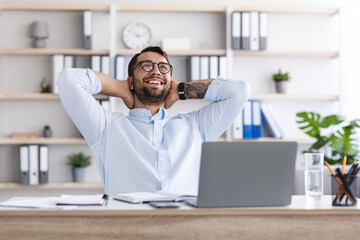 Satisfied middle aged caucasian guy with beard in glasses resting from work at laptop