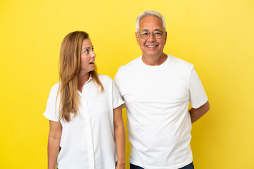 Middle age couple isolated on yellow background with surprise facial expression
