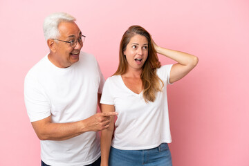 Middle age couple isolated on pink background pointing finger to the side with a surprised face