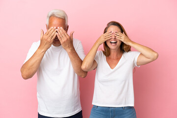 Middle age couple isolated on pink background covering eyes by hands