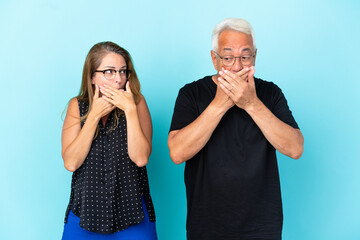 Middle age couple isolated on blue background covering mouth with hands