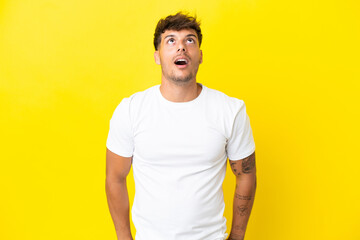 Young caucasian handsome man isolated on yellow background looking up and with surprised expression