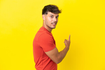 Young caucasian handsome man isolated on yellow background pointing back