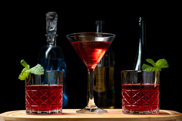 three cacktail red, royal drink on a wooden board bottles of drinks blurred in the background, on a dark background