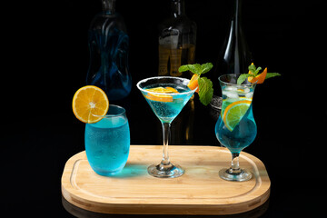 three cacktail blue, curaçao blue on a wooden board bottles of drinks blurred in the background, on a dark background
