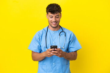 Young surgeon doctor man isolated on yellow background sending a message with the mobile