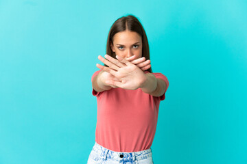 Young woman over isolated blue background making stop gesture with her hand to stop an act