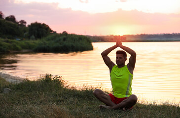 Fototapeta na wymiar Man meditating near river at sunset. Space for text