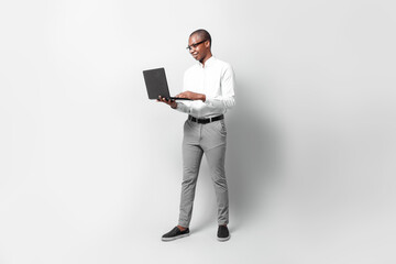 Full length of black young business man holding a laptop over gray background professional concept.