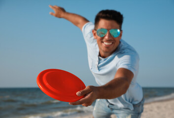 Happy man throwing flying disk at beach, focus on hand