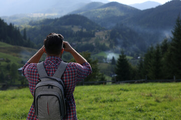 Tourist with backpack and binoculars enjoying landscape in mountains, back view