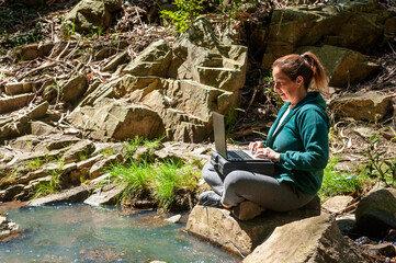 woman with cell phone and notebook laptop chatting on top of a mountain very relaxed contemplating the landscape