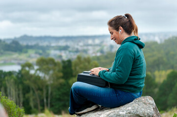 Naklejka na ściany i meble woman with cell phone and notebook laptop chatting on top of a mountain very relaxed contemplating the landscape