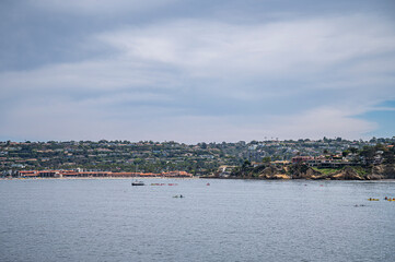 Fototapeta na wymiar La Jolla, California, USA - October 3, 2021: Wide veiw from Point La Jolla on red roofed beach and tennis club along water with green belt of housing separating blue cloudscape from ocean.