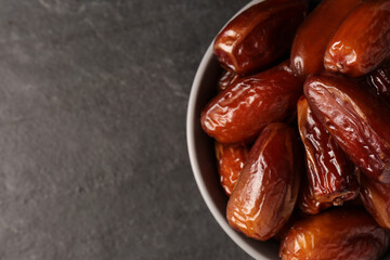 Tasty sweet dried dates in bowl on black table, top view. Space for text
