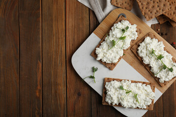 Crispy crackers with cottage cheese and microgreens on wooden table, flat lay. Space for text