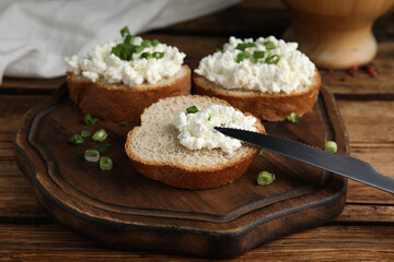 Bread with cottage cheese and green onion on wooden table, closeup