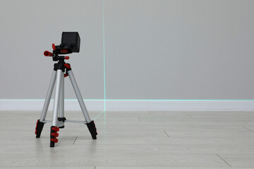 Cross line laser level on tripod in front of light wall indoors