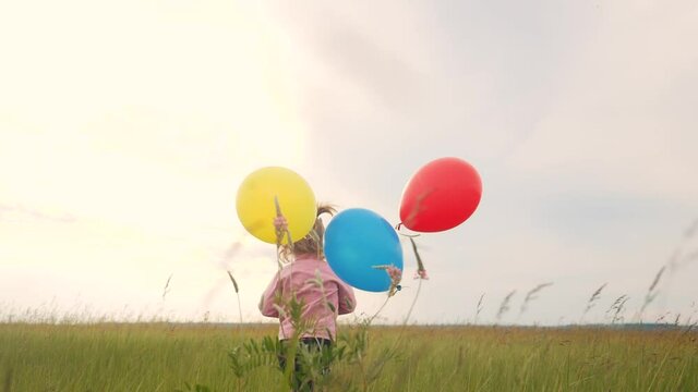 daughter little girl fun runs with balloons a on her birthday outdoors by field. dream happy family concept. child girl kid day. child is running and balloons on a background of lifestyle blue sky