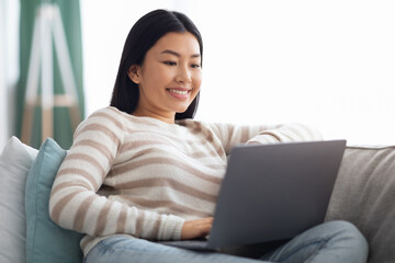 Naklejka premium Freelance Job. Closeup Of Young Asian Woman Sitting On Couch With Laptop